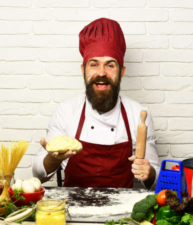 Cook with happy face in burgundy uniform sits by tableの写真素材