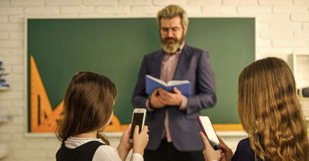Problem of smartphones in schools. Have fun with smartphone instead studying. Internet addiction. Addicted to internet online games. Internet surfing social networks. School students and teacherの写真素材
