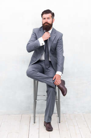 With lofty ambitions. Brutal man in elegant suit. Bearded man with formal look. Hipster sit on chair. Man with mustache and beard hair. Everyday office wear for busy man. Fashion and styleの写真素材