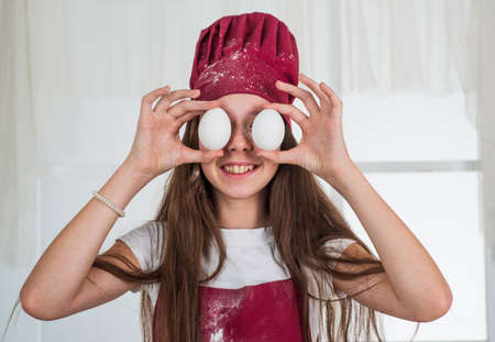 oh my god. small girl baking in kitchen. kid chef cooking with eggs. child prepare healthy food at home and wearing cook uniform. housekeeping and home helping. childhood developmentの写真素材