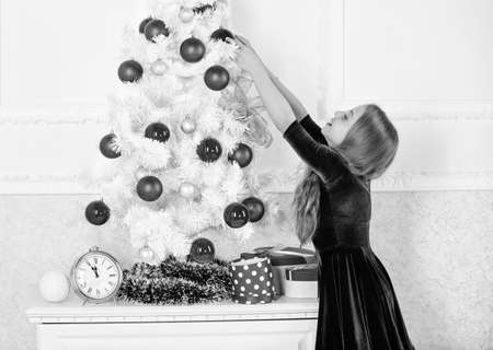 Child hang christmas ornament ball on artificial tree. Kids can brighten up christmas tree by creating their own ornaments. Girl celebrate christmas. Top christmas decorating ideas for kids roomの写真素材
