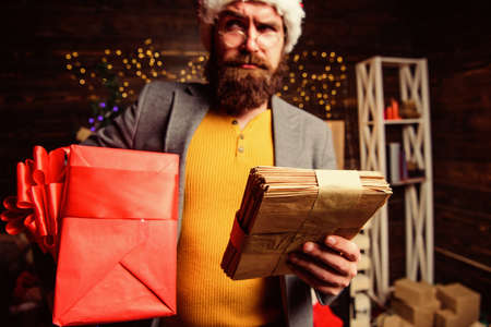 Man mature bearded with eyeglasses received post for santa. Gifts delivery service. Post for santa claus. Man bearded hipster wear santa hat hold bunch of letters and gift box. Letter for santa clausの写真素材