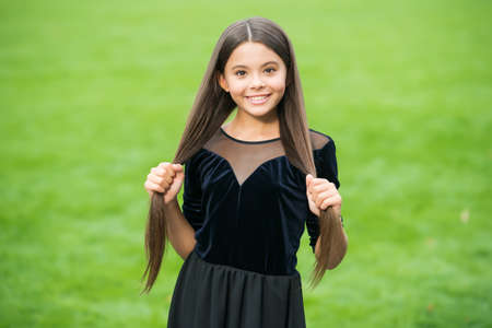 Happy small girl with beauty look smile holding long brunette hair in fashion dress green grass...
