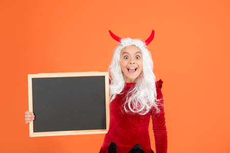 surprised witch kid has white hair hold school balckboard for announcement wear costume horns of imp...