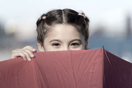 Playing hide and seek. Funny young girl hiding from somebody. Beautiful bright eyes. Girl with umbrella playing game. Having funny mood. Childhood without problems and troubles. Playing outsideの写真素材
