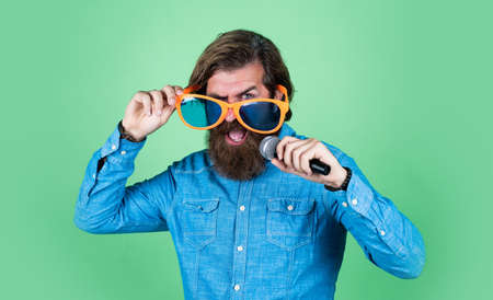 Music chose me. have some fun. birthday party singer. celebrate the holiday. hipster singing a song. music. happy bearded man wear funny party glasses. mature event manager hold microphoneの写真素材
