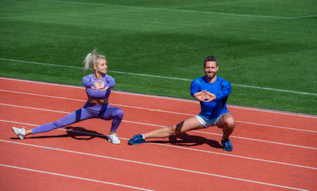 fitness sport couple warming up and stretching together on outdoor stadium racetrack wearing...