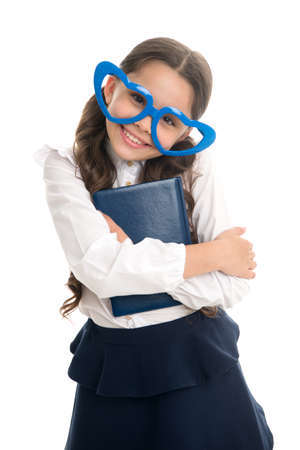 Schoolgirl heart shaped glasses isolated white background. Child girl school uniform clothes hugs book. Child wear school uniform kid happy face. Reading her favorite lesson. Literature her hobbyの写真素材