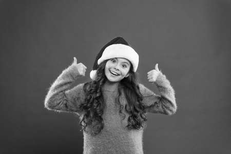 having fun on best party. little santa. feeling happy about new year. time for christmas holiday. small girl in santa hat. cheerful child red background. winter kid fashion. favorite winter holidayの写真素材