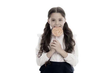 Enjoying delicious candy. Girl cute kid ponytails hairstyle eats sweet lollipop. Sweets in appropriate portions ok. Girl pupil school uniform likes sweets lollipop candy isolated white backgroundの写真素材