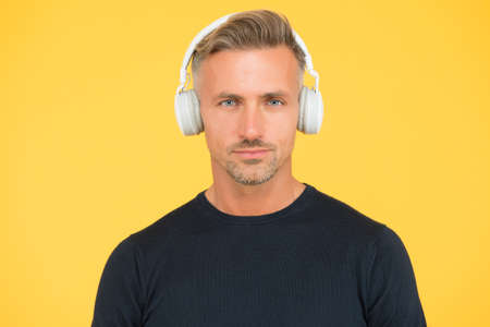stylish mature guy with trendy hairstyle wearing earphones listening to ebook or audio book for...