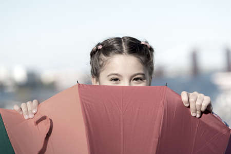 Hiding from problems. Positive and bright. Girl cute child standing with colorful umbrella. Child behind umbrella. Colorful accessory for cheerful mood. She likes bright accessories. Umbrella for kidの写真素材