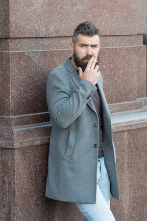 mature hipster with beard smoking cigarette. addiction. brutal caucasian hipster with moustache. male bad habits. casual fashion in modern life. confident and handsome brutal man. smokeの写真素材