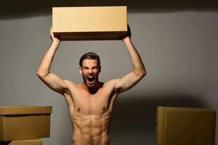 Guy with sexy naked torso holds box above head.の写真素材