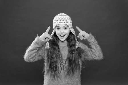 Wintertime concept. Little kid wear knitted hat. Little girl winter fashion accessory. Small child long hair wear hat red background. Frosty weather. Winter outfit. Cute model enjoy winter styleの写真素材