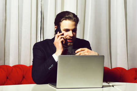 bearded man, businessman holding glass of whiskey works at laptopの写真素材