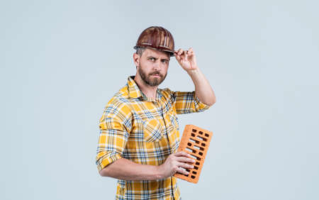 handsome man manual worker in construction safety helmet and checkered shirt on building site with brick, reconstructionの写真素材