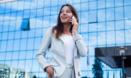 A beautiful young happy business lady standing in city street and speaking on mobile phone,...