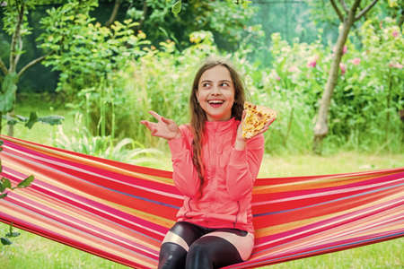 Riding in a hammock. happy childhood. child feel hunger. hungry kid going to eat italian pizza. fast food. happy childrens day. little girl eating pizza. pizza delivery. unhealthy and healthy foodの写真素材