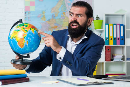 Leaning and playing. informal education. male student sit in school classroom with map. pass the exam. learning the subject. geographer. confused man with beard look at globe. geography studyingの写真素材