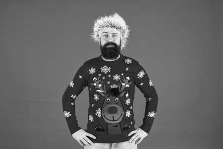 Christmas party time. cold weather fashion for men. happy new year. bearded man on red wall. funny man with beard in knitted sweater. pazzled hipster ready for xmas party. winter holiday celebrationの写真素材