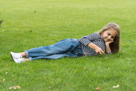 Cute little kid wear casual fashion style lying on green grass natural landscape, summerの写真素材