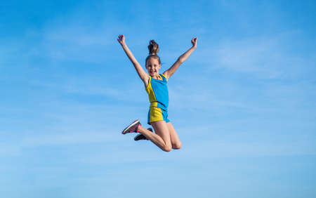 stretching and warming up. childhood happiness. health and fitness. gymnastics. sense of freedom. happy teen girl jump on sky background. kid has flexible body. child in sport clothes trainingの写真素材