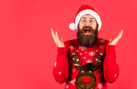 Finding perfect present. Bearded man santa hat. Emotional hipster winter knitted sweater red background. Winter holiday fun. Santa man. New year party. Christmas time. Have fun. Promoting goodsの写真素材
