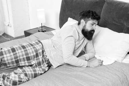 Hard to wake up. bearded man hipster want to sleep in morning. brutal sleepy man in bedroom. mature male with beard in pajama on bed. asleep and awake. energy and tiredness. wake up not todayの写真素材