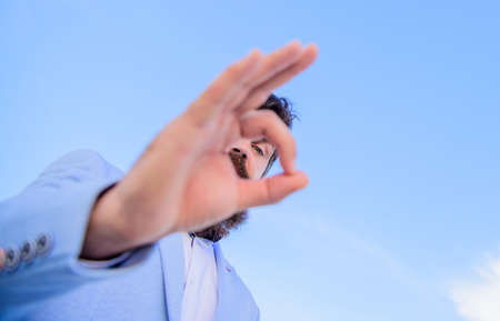Guy looks through ok gesture close up. Excellent concept. Spying watching and observing. Man bearded businessman formal suit watching through fingers. I am watching you. Perfect gestureの写真素材