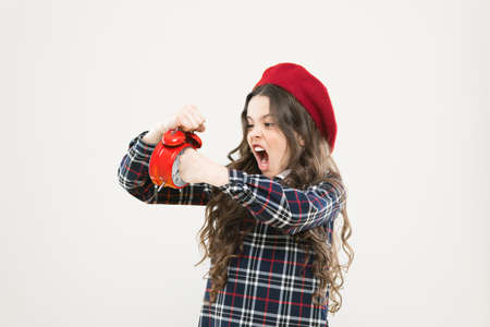 She is late for school. Small child punching alarm clock with anger on yellow background. Angry little girl fighting with late hour. Hurry up its too lateの写真素材