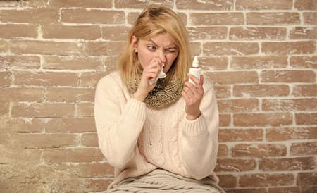 Reading instruction on label. Cute woman nursing nasal cold or allergy. Sick woman with nose drops. Pretty girl with runny nose holding nasal drops. Suffering from asthma or allergic rhinitisの写真素材