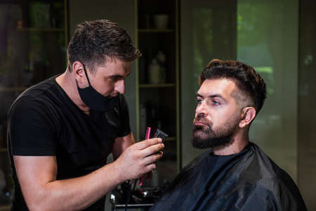 attractive barber making haircut of handsome guy in barbershop, hairdressing toolsの写真素材