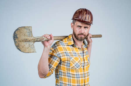 handsome man expert in construction safety helmet and checkered shirt on building site with shovel,...