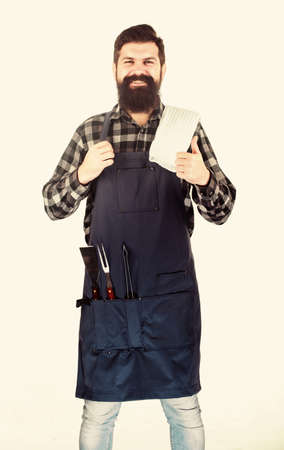 Barbecue season. Bearded hipster wear apron for barbecue. Roasting and grilling food. Tips for cooking meat. Man hold cooking utensils barbecue. Tools for roasting meat outdoors. Picnic and barbecueの写真素材