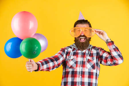 Young and carefree. Party Elements and holiday objects. Multi colored fun. best party for retirement. cheerful man with beard and moustache. hipster smiling with balloon. Celebrating happy partyの写真素材