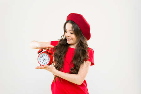 happy girl with long curly hair in beret. child with alarm clock. Timeless fashion. parisian child...