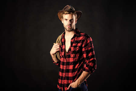 Cowboy wearing hat hold rope. Lasso tool of American cowboy. Still used on ranches to capture cattle or other livestock. Western life. Lassoing on prairie. Man unshaven cowboy black backgroundの写真素材