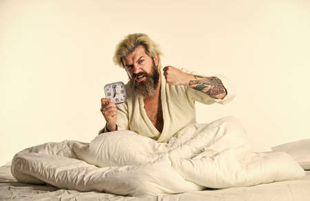 bedtime. Destroy the Clock. handsome angry man lies in bed indoors wake up turn off the alarm clock.