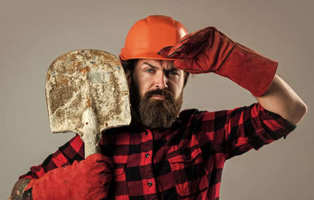 Man at work. wearing safety gear. supervisor at construction site. confident serviceman. brutal hipster man. man in hard hat. engineer use shovel in gloves. construction worker wear safety helmetの写真素材