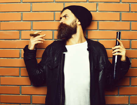 Bearded brutal caucasian hipster holding bottle and smoking cigarの写真素材
