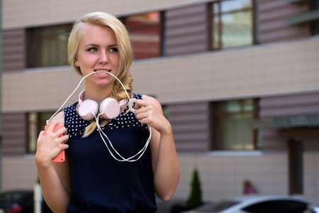 Woman with blonde hair hold wire of headphones in teethの写真素材