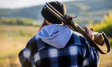 Brutality and masculinity. Hunter carry rifle gun on shoulder rear view. Guy hunter spend leisure hunting. Hunting masculine hobby leisure concept. Man brutal guy gamekeeper in hat nature backgroundの写真素材