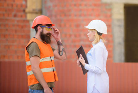 Construction industry concept. Woman engineer and bearded brutal builder discuss construction...