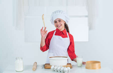 making cake by recipe. time to eat. happy child cooking in kitchen. bake cookies in kitchen. professional and skilled baker. kid in chef uniform and hat. teen girl preparing doughの写真素材