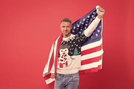 My motherland. Mature man hold american flag. Handsome man celebrate winter holidays red background. Guy wear winter sweater. Merry christmas and happy new year. Best wishes. Winter vacationの写真素材