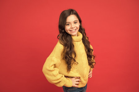 perfect hair after hairdresser. small beauty red background. pretty girl long curly hair. happy little girl knitted sweater. fashion for kids. autumn and winter warm clothes. warm wear any seasonの写真素材