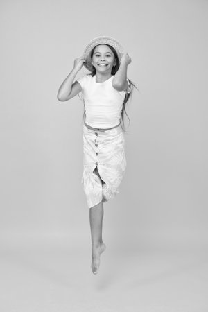 jumping fidget. small girl wear summer outfit. summer vacation fashion. happy childrens day. having fun on beach party. kid in straw hat. happy barefoot child jump. carefree childhood happinessの写真素材