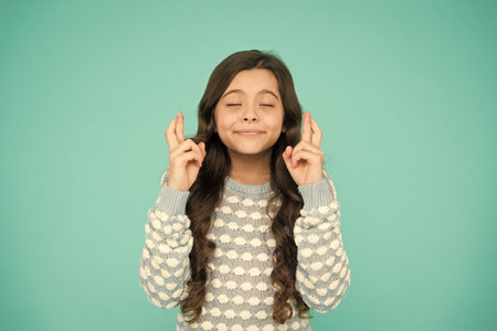 Full of hope. Child dream. Hopeful concept. Small child with long hair. Hope for best. Little child keep fingers crossed for luck. Believe in herself. Cute child make wish turquoise backgroundの写真素材