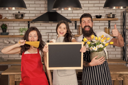 Family restaurant concept. Teach kid cooking food. Cooking together. Recipe copy space. Best cooking team. Mom dad and daughter aprons in kitchen. Lunch time. Family having fun cooking togetherの写真素材